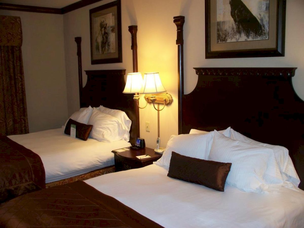 The image shows a hotel room with two double beds, decorated with white linens and brown accent pillows, along with a bedside lamp and wall art ending the sentence.
