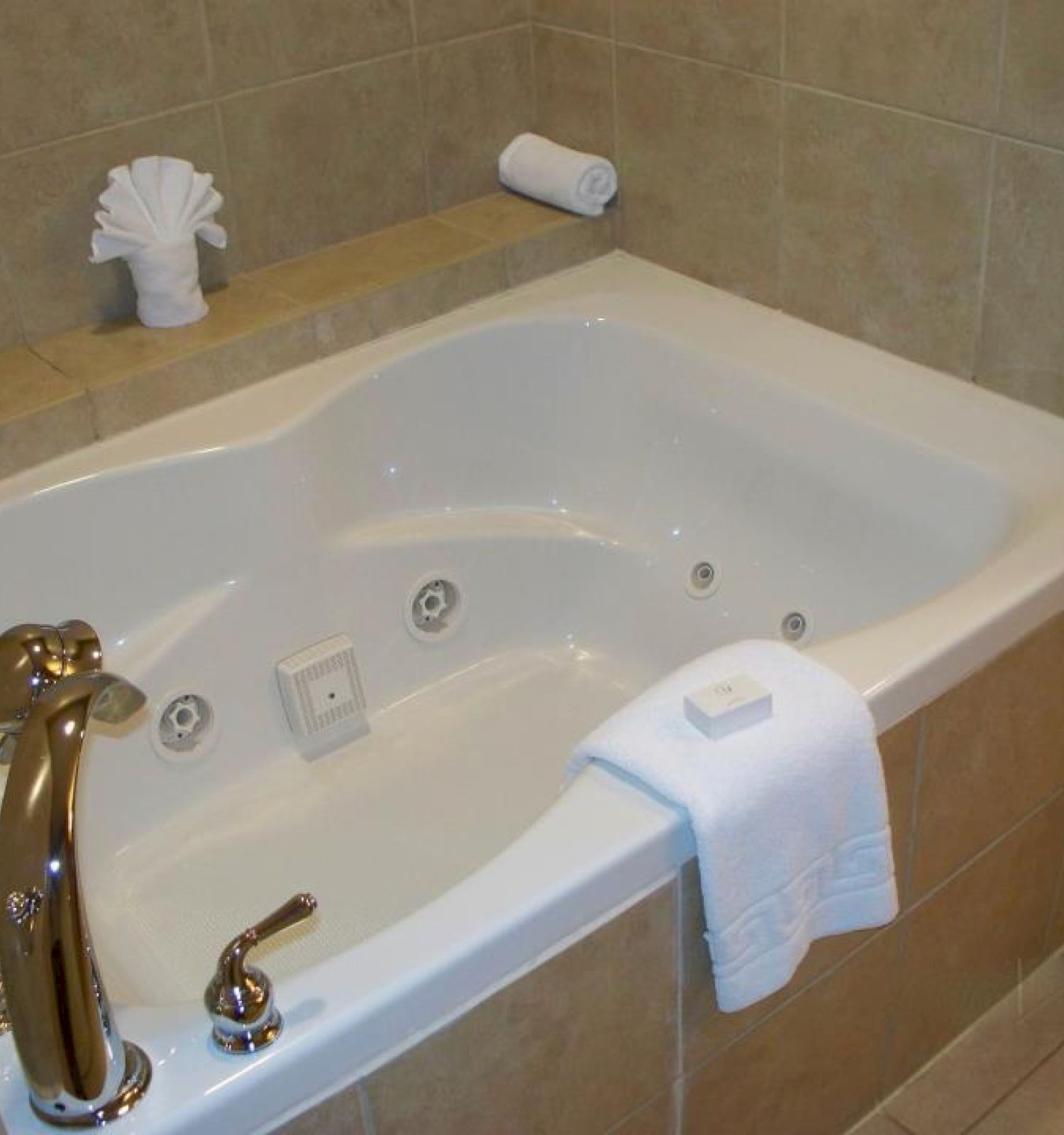 A bathroom with a jetted bathtub, folded towel, bar of soap, and a roll of toilet paper. The tub has golden faucets.