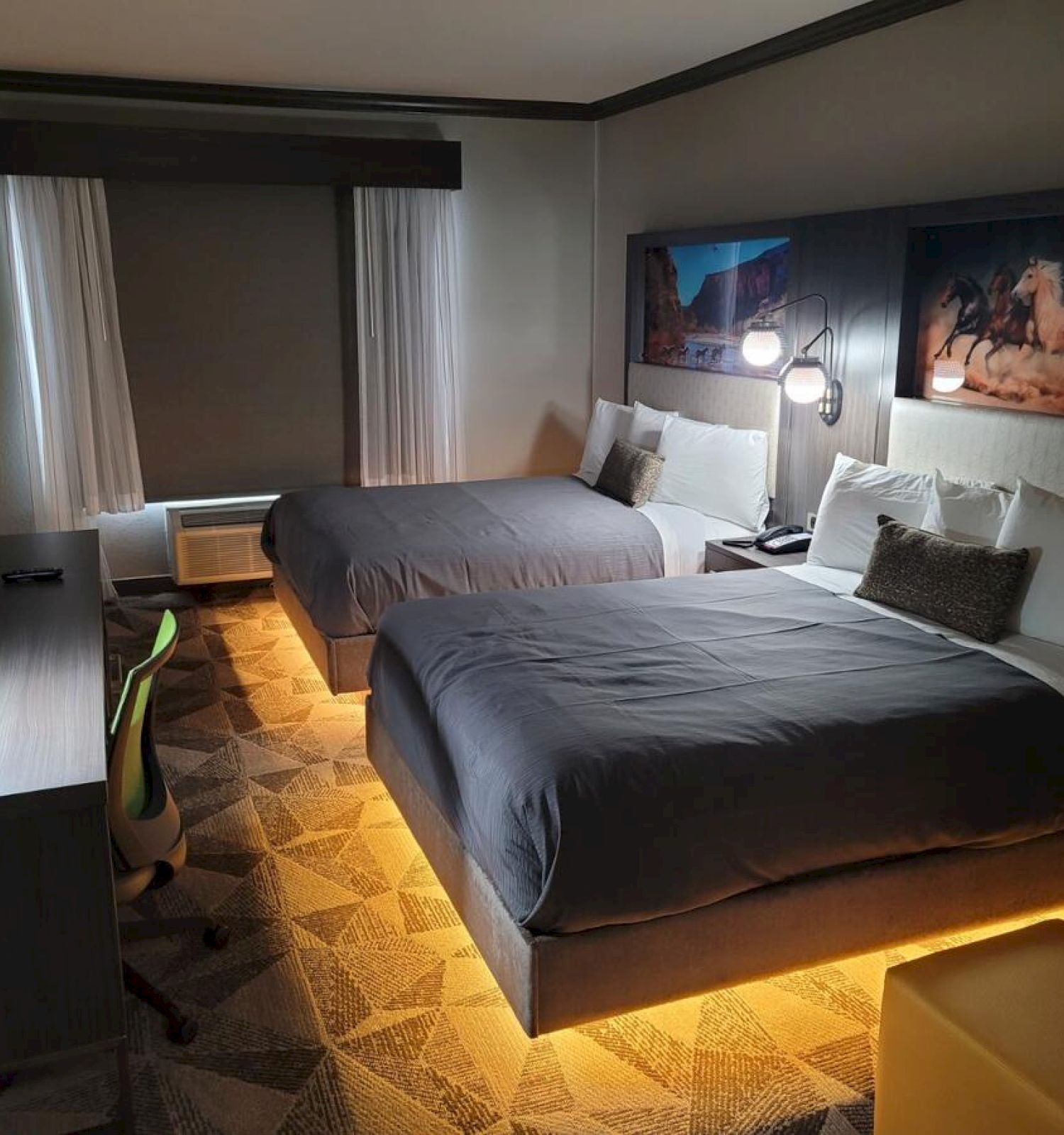 The image shows a modern hotel room with two beds, nightstands, a desk with a chair, a TV, and a painting above the beds.