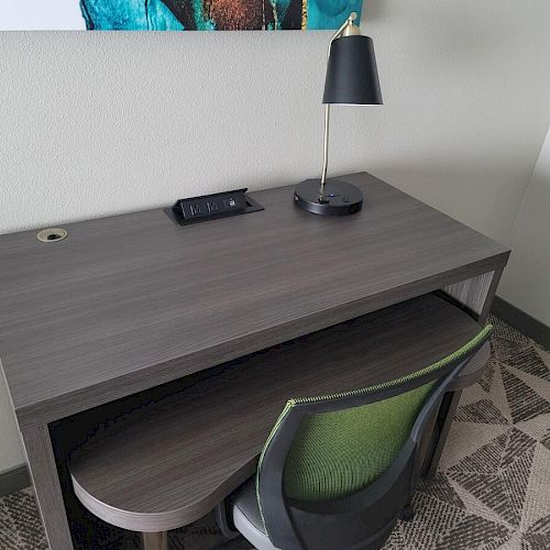 The image shows a desk with a lamp, a remote control, and a green-back chair. The desk is located in a room with patterned flooring.